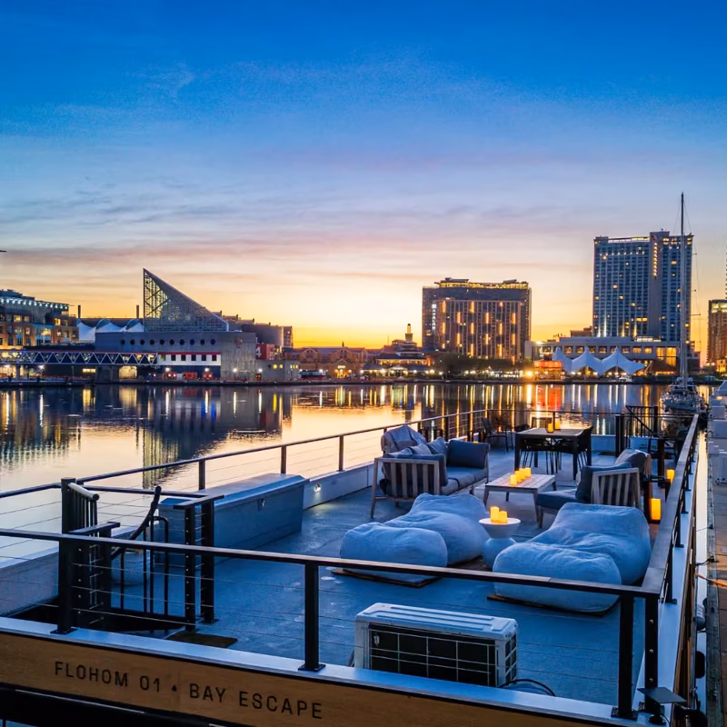 FLOHOM rooftop deck at dusk with lounge seating, overlooking the harbor skyline