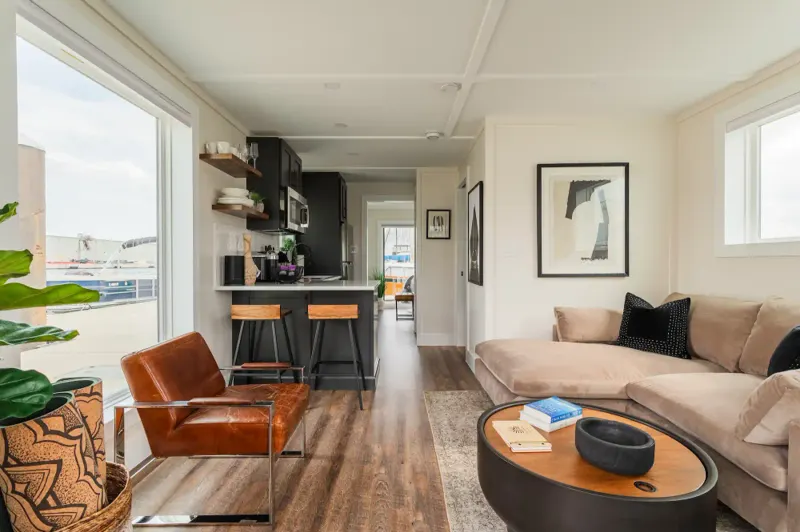 FLOHOM living room with tan sectional, cognac leather armchair, and kitchenette, dock and boats out the window