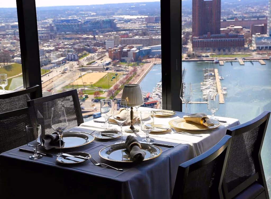 A set dinner table beside a window overlooking the Baltimore harbor and marina below.