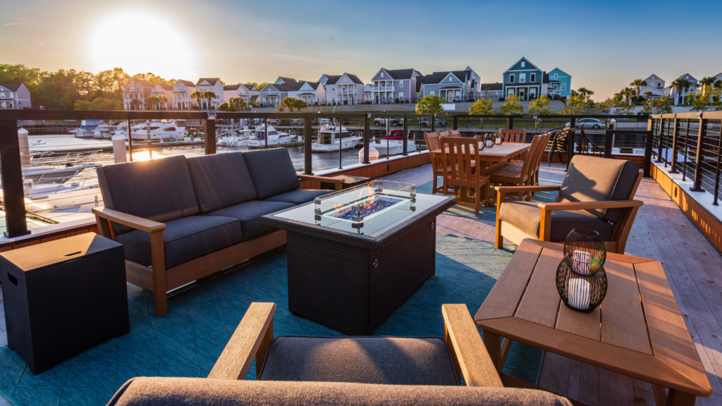 Rooftop deck of FLOHOM 15 Palmera at sunset with fire pit, outdoor sofa, teak dining table, and views of Barefoot Landing Marina on the Intracoastal Waterway.