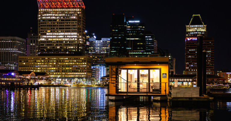FLOHOM 1 Bay Escape floating suite illuminated at night on Baltimore's Inner Harbor with city skyline in background