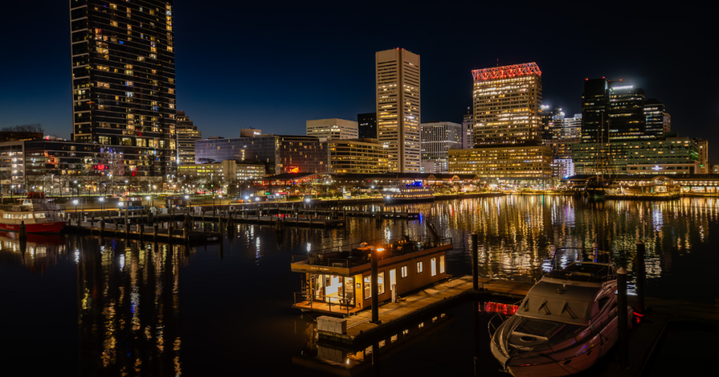 FLOHOM 1 Bay Escape floating suite docked at Baltimore Inner Harbor Marina at night with downtown city skyline in background